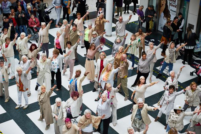 A large group of older dancers performing at White Rose Shopping Centre, viewed from overhead.
