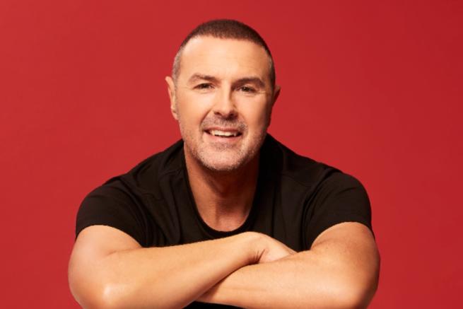 Paddy McGuinness smiling with a rusty red background.