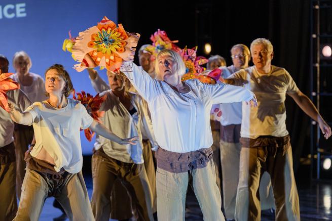 Dancers from Ascendance reach to the sky, holding large brightly coloured paper flowers