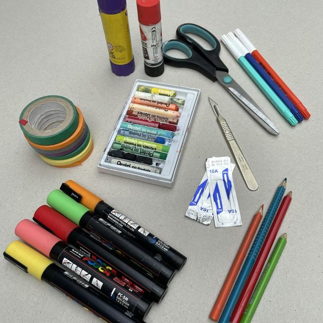 A selection of pens, pencils, scissors, glue and coloured tape are laid on a desk