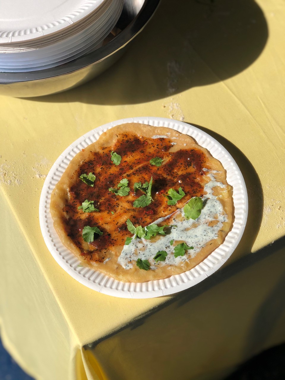 Picture shows a paper plate with a traditional Punjabi potato flatbread coated in sauces and corriander plated on a table 