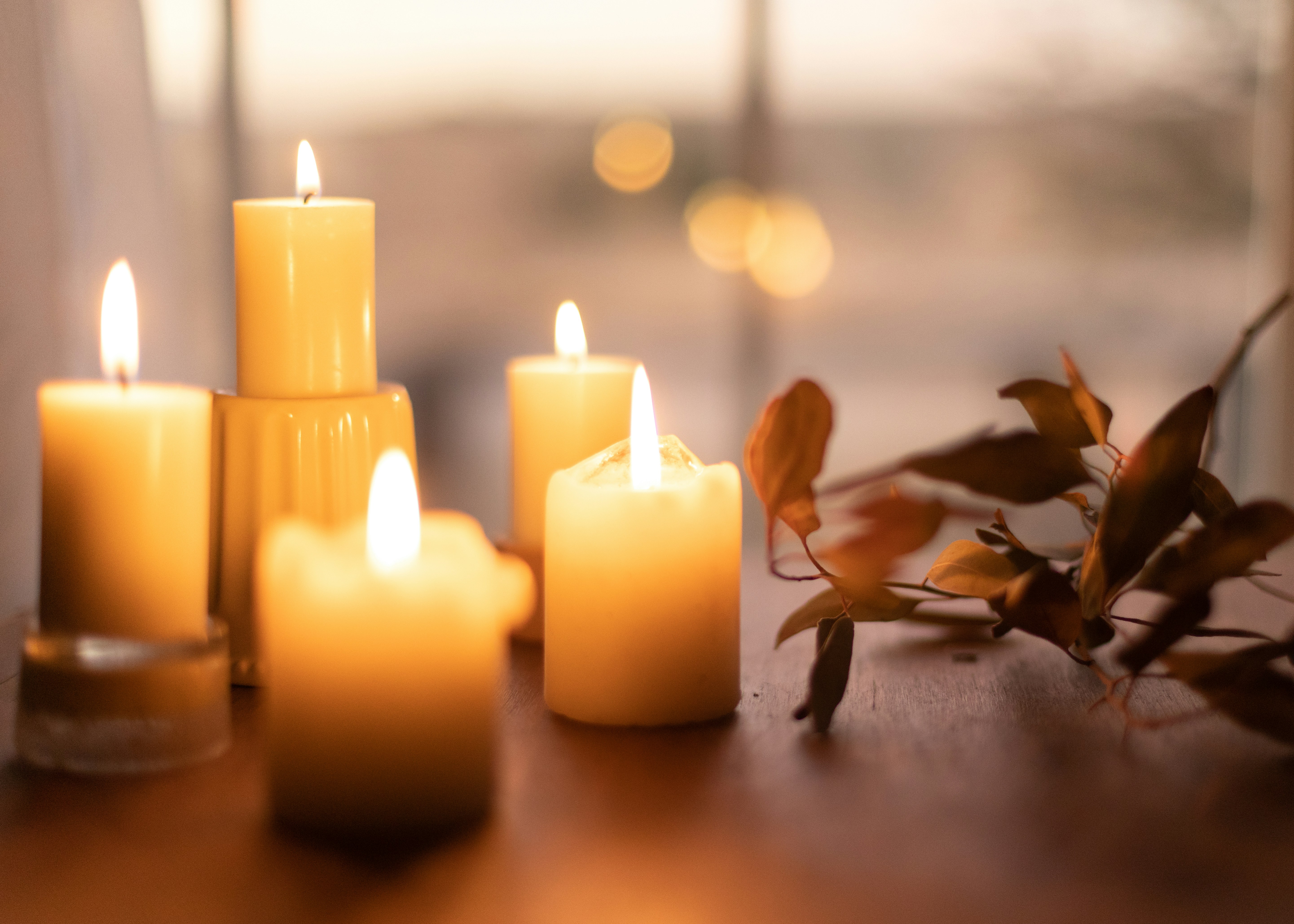 Five lit candles in front of a window next to some leaves