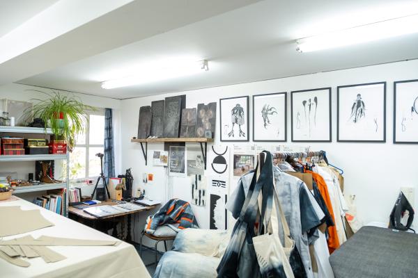 An artist studio can be seen, with textiles hung on a clothes rail, and images hung along a white wall