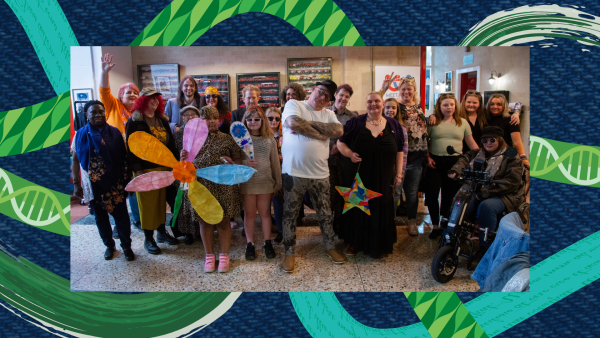 Blue background with 5 wiggly lines. One line is green and paint-like, one line is green with a leaf print, one line is teal with writing, one line is teal and green with dna strands, and one line is blue and has a gingham pattern. On top of the lines is a picture of a group of people at a community event, some hold colourful lanterns and crafts. They are all posing and looking at the camera.