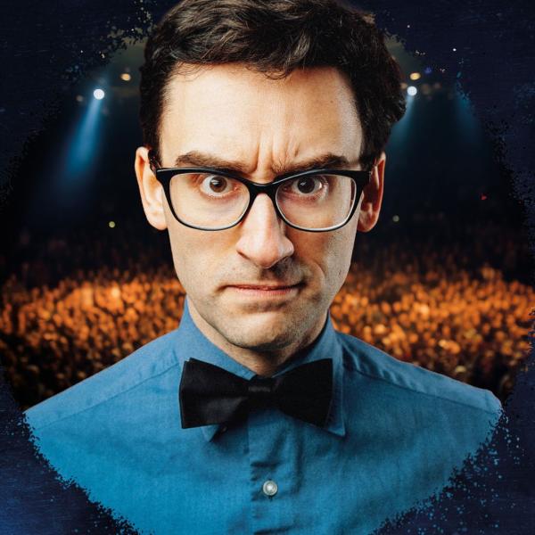 MC Hammersmith with a bowtie and glasses, in front of a crowd. 