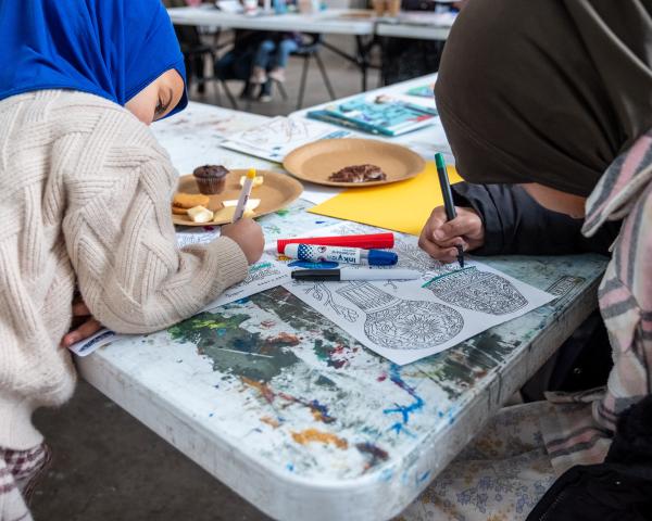 Young people are drawing onto some pottery designs at a messy table space.