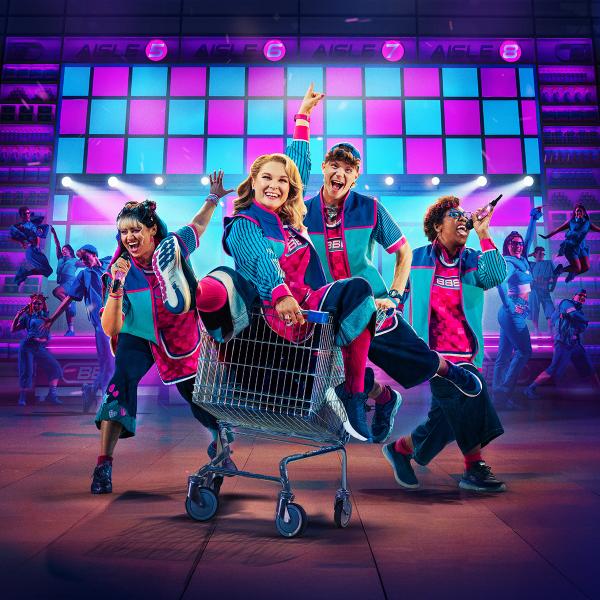 Promotional image for Here & Now. Four singing and dancing characters in matching blue and pink supermarket uniforms, as one of them sits in a moving shopping trolley, in front of neon lights and backing dancers. 