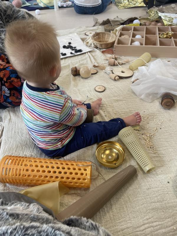 A baby sat on a blanket playing with a variety of textured materials and objects.