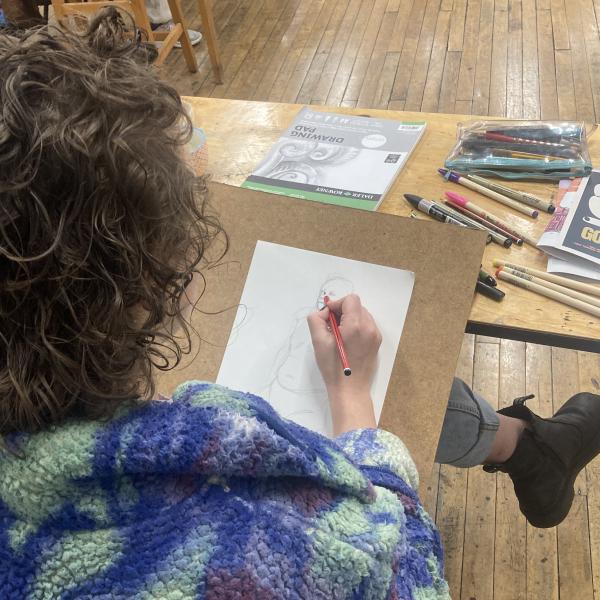  A photograph taken over a persons shoulder as they are drawing a figure on a piece of white paper