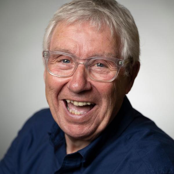 Gregor Fisher smiles at the camera in front of a plain grey background.