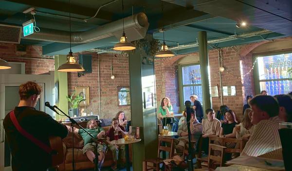 A person is playing guitar with their back to the camera, a crowd is watching.