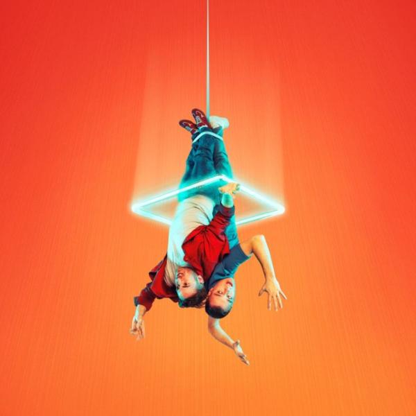 Two people dangle upside-down from a rope around their ankles, encased in a bright neon light against an orange background. 