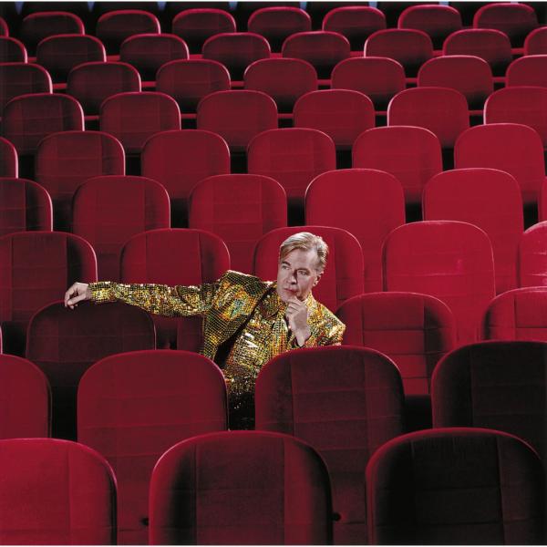 Martin Fry sat in a middle row of some traditional red theatre or cinema auditorium seats.