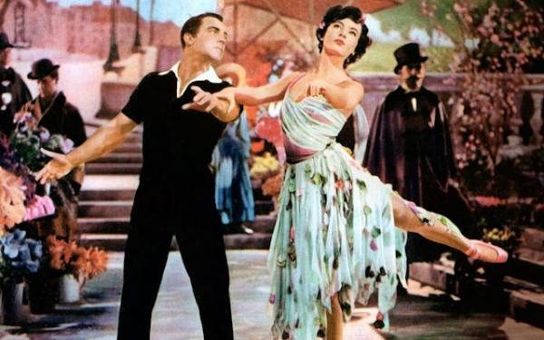 Two people dancing. The man is wearing black, the woman a colourful dress.