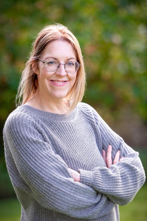 Author Dr Ellen Welch stands facing camera smiling, with arms crossed.