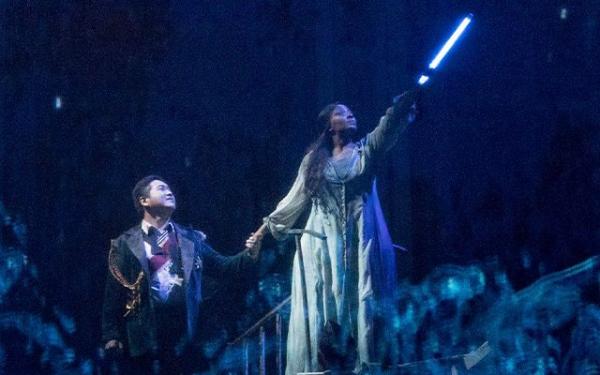 A woman in a dress holding a long light. She is holding hands with a man who is kneeling.