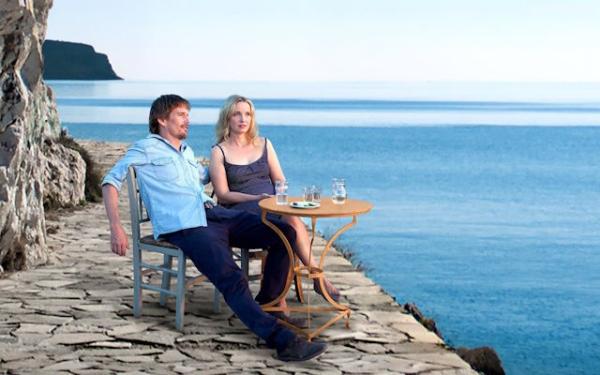 A man in a blue shirt sat next to a woman in a dress looking at the ocean.