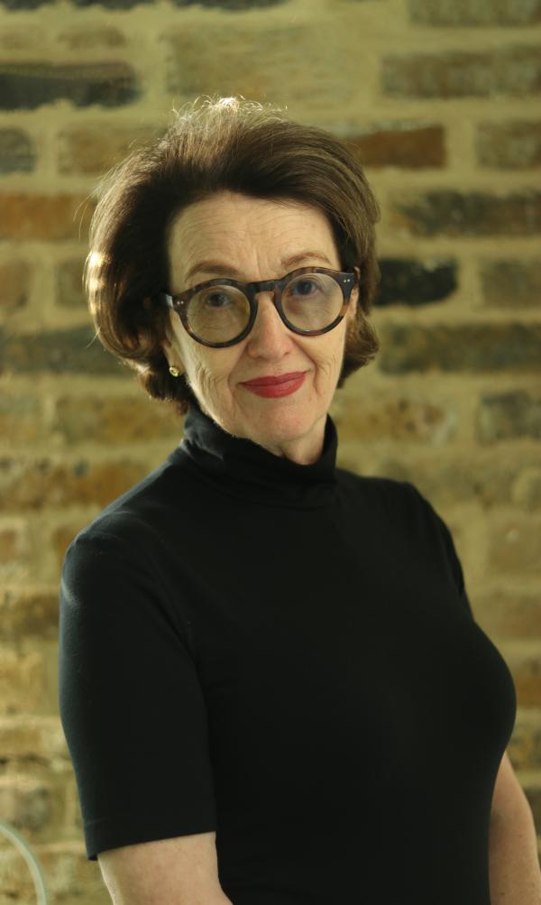 The author Monique Charlesworth stands facing camera in front of bricked wall.