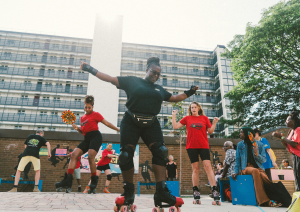 A group of women dancing on rollerskates in a brightly coloured community garden 