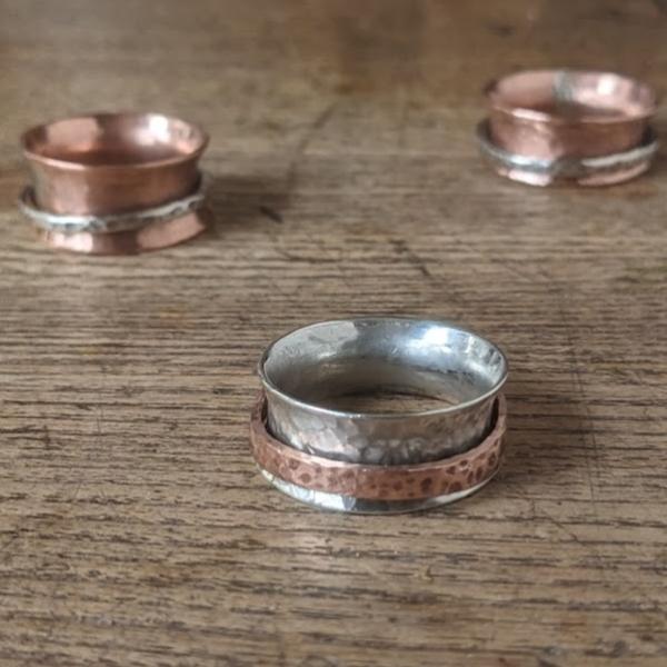 three silver and copper spinning rings lay on a wooden table