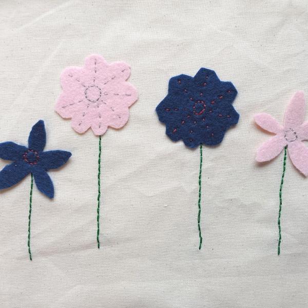 4 applique flowers in blue and pink are stitched onto a cream background fabric