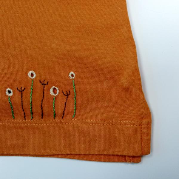 An orange top with stitched flowers