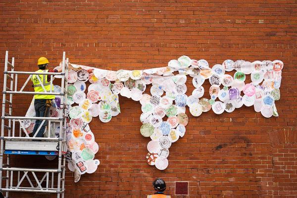 Man in hi vis and hard hat installing large fabric artwork on a brick wall.