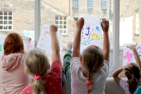 group of children lean against inside of window drawing on clear plastic sheet with poca pens