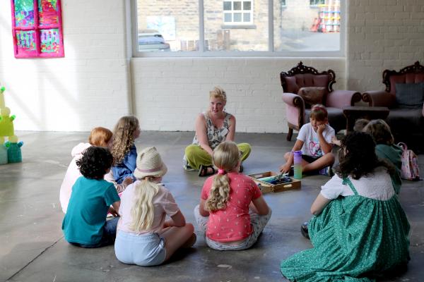 Group of children and adults sit in a circle on the floor in the gallery space 