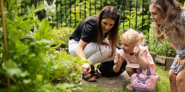 image showing two children crouched in a garden with an older woman