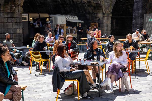 Image shows people sat around tables in the sun