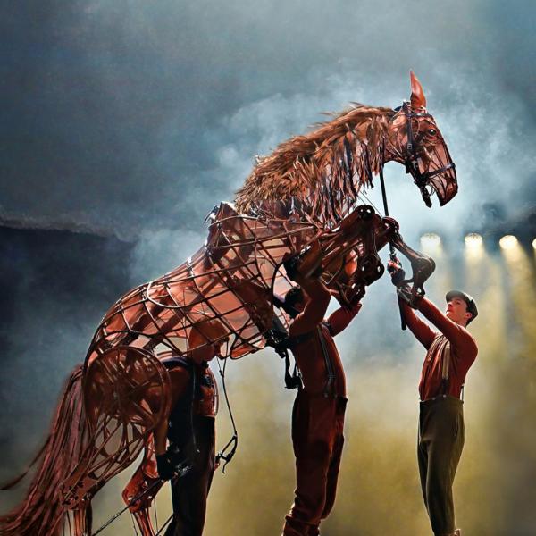 Life-size horse puppet on its hind legs being operated by three puppeteers.