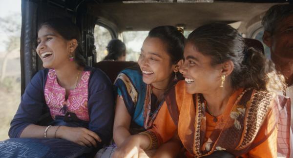 Three women laughing together in the back of a vehicle.