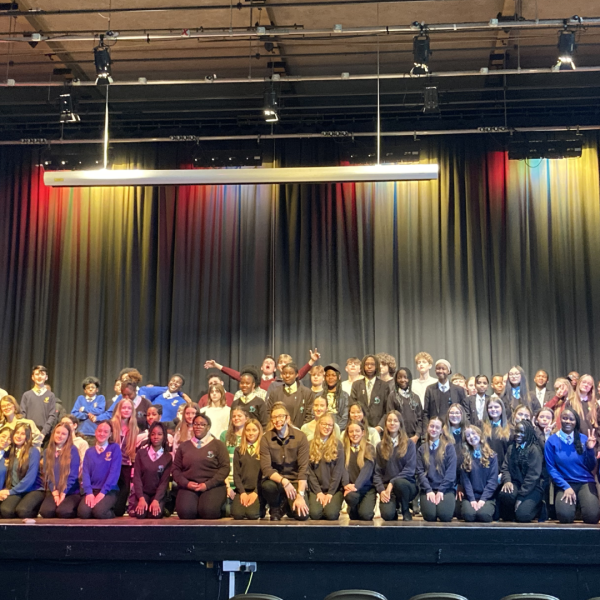 Secondary school pupils on a stage with Craig Lee with multi-coloured spotlights on them.