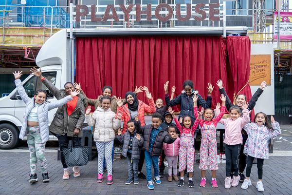 A group of people in front of  a white van with theatre curtains. They seem happy with their arms raised.