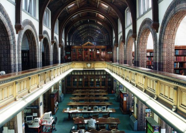 View of the reading room at Central Library. There are long tables and chairs with a gallery running around the room.