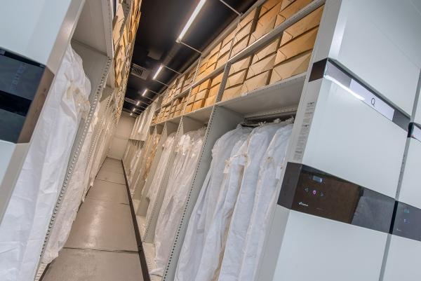 A colour photo of Archive shelving full of boxes and clothing in protective bags.