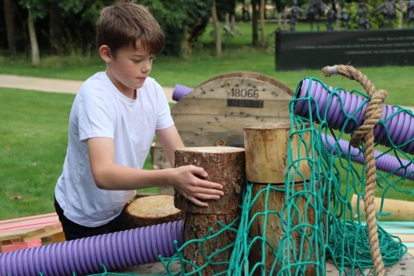 A young boy happily playing with a wooden structure in a park.