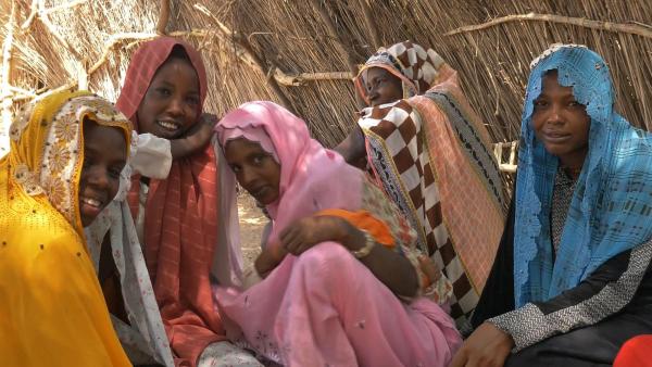 Five women with brightly coloured head-scarves look into camera smiling 