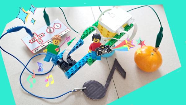 A Lego Spike kit and mini-figure wired to a Makey Makey and orange