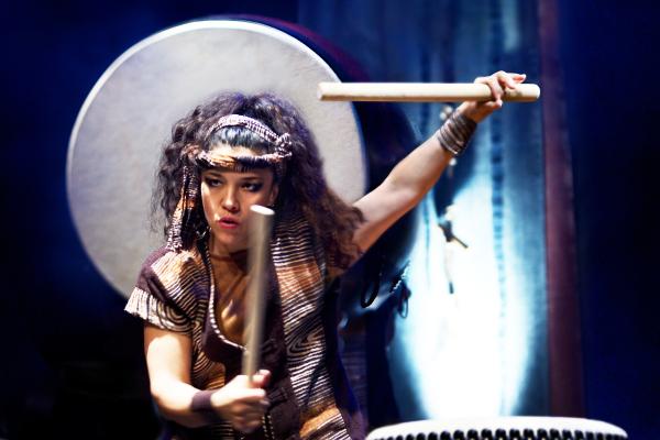 A person holding two large sticks aloft above a drum.