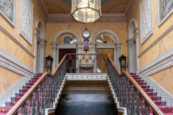 A large grand staircase with a clock on the wall at the top showing the time.