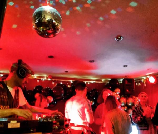 A blurry photo of a DJ playing to a crowd of revellers underneath a mirror ball.