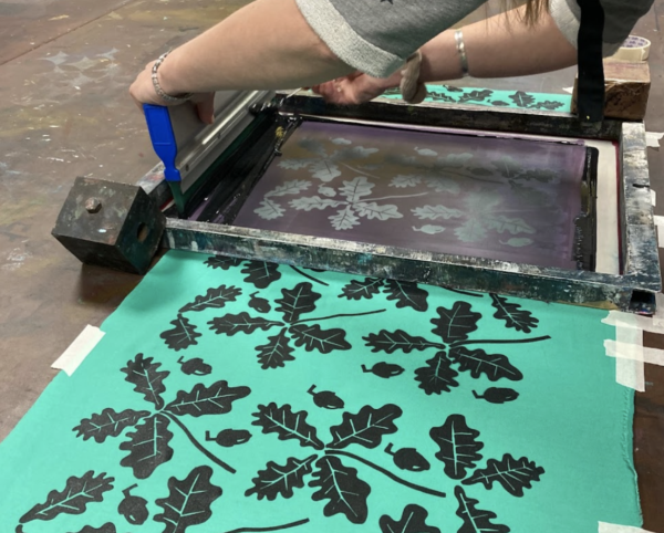 A repeat leaf pattern being screen printed in black ink on green fabric
