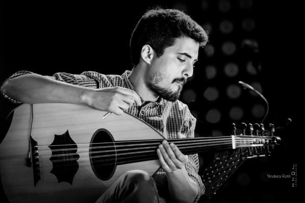 Black and white photo of the musician playing the oud, which looks similar to a guitar