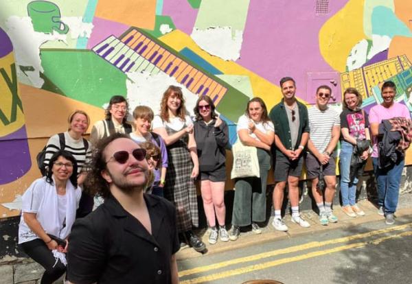 A group of people stand in front of a bright wall mural