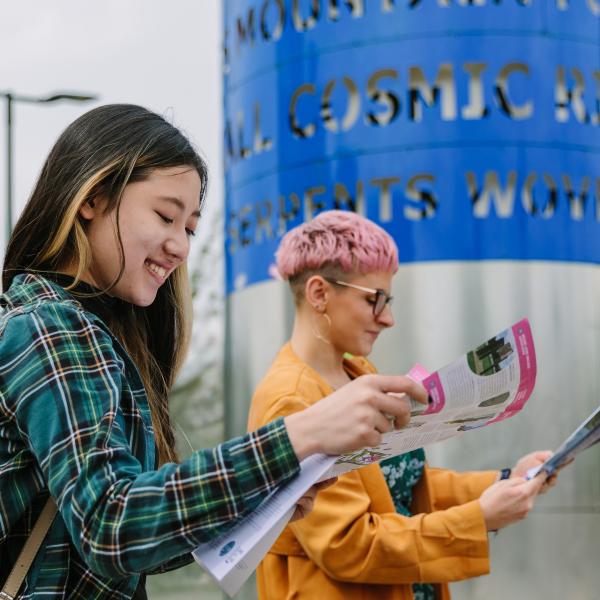 Two people holding Public Art maps stood beside a blue and silver cylindrical sculpture