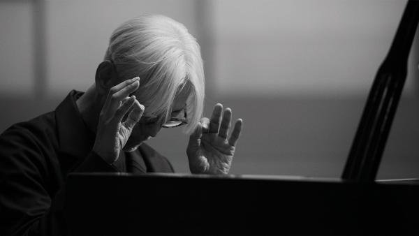 Black and white image of Ryuichi Sakamoto playing piano.