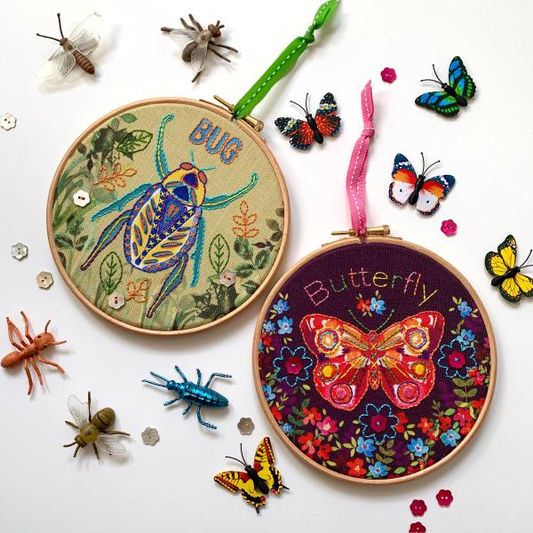 two embroidery hoops one with a beetle design and one with a butterfly design.