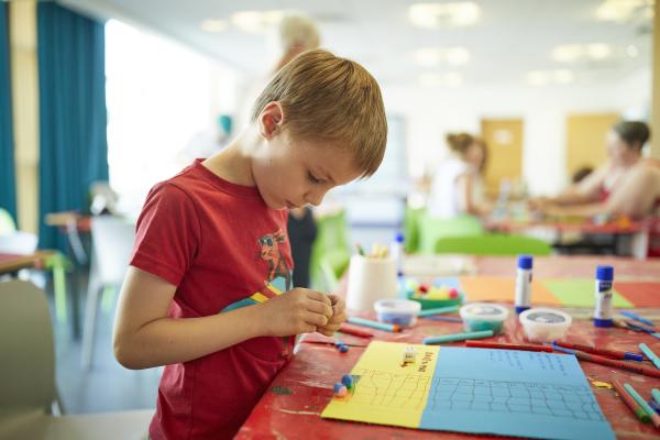 Boy in red t-shirt making his own boardgame using paper 